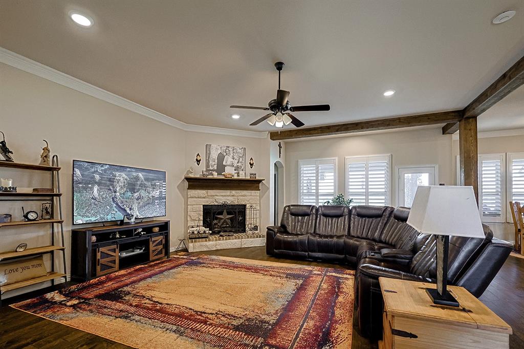 Living area featuring stone-surround corner fireplace with timber mantel, recessed lighting, ceiling fan, crown molding, and plantation shutters