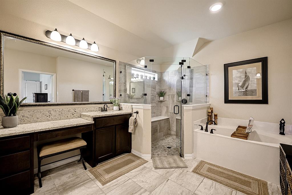 Bathroom featuring a dual-sink vanity with stone countertops, a frameless glass-enclosed shower with tile surround and built-in bench, a deep soaking tub, and tile flooring