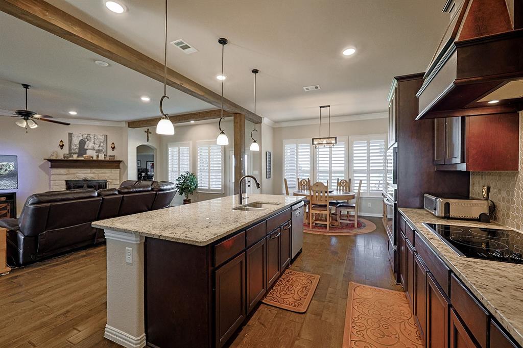 Stone fireplace with wooden mantel, wood-finish flooring, exposed wooden ceiling beams, recessed lighting, and wooden cabinetry