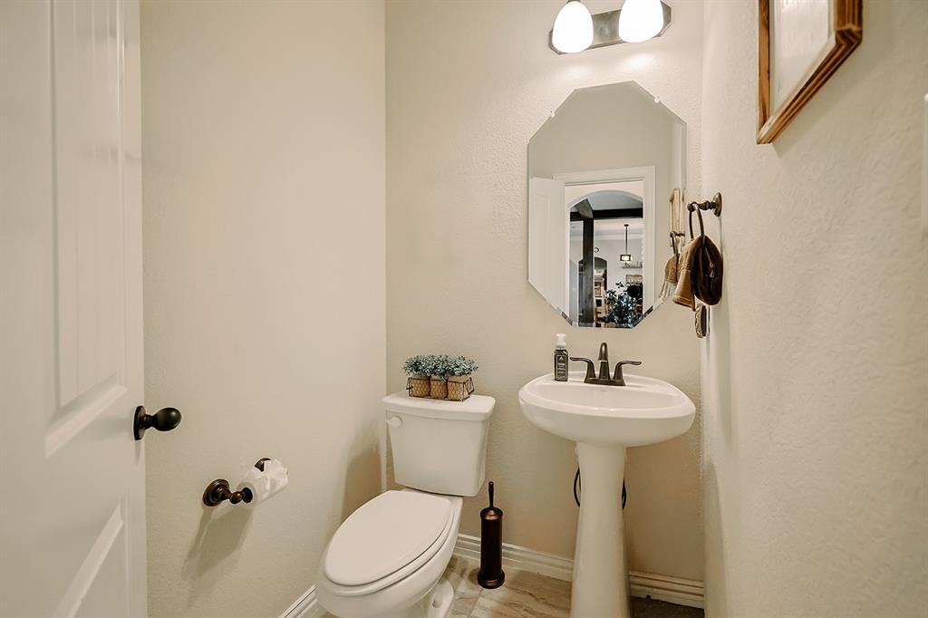Powder room featuring a porcelain pedestal sink, dual-handle oil-rubbed bronze faucet, octagonal wall mirror, and two-light vanity fixture