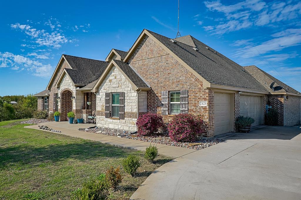 Multi-gable brick and stone exterior featuring decorative shutters, a concrete driveway, and an attached two-car garage