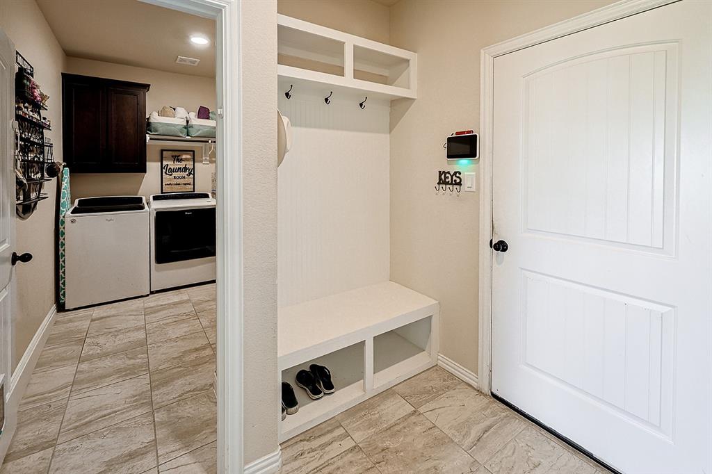 Mudroom area featuring built-in cabinetry with bench seating and overhead storage, tile flooring, and dark wood-finish wall cabinets