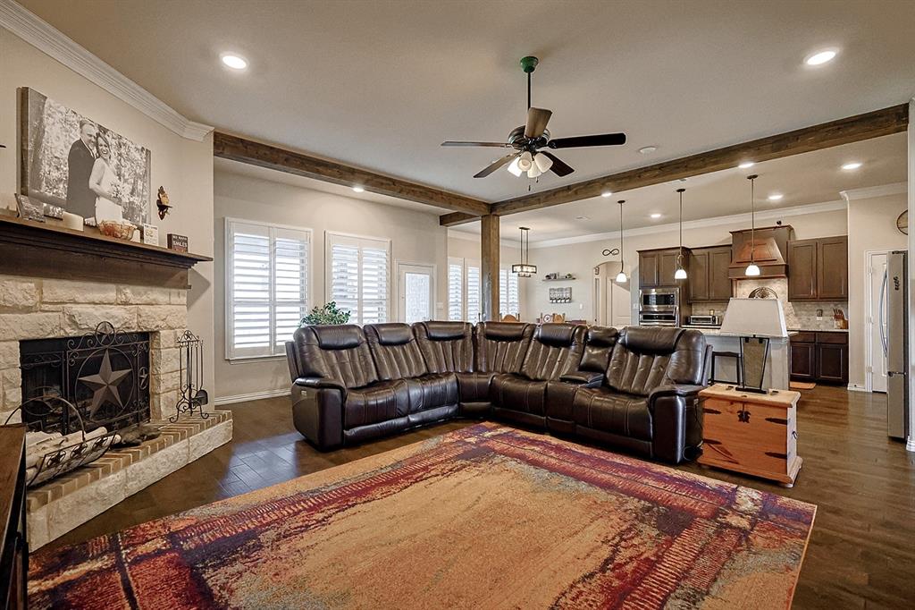 Stone fireplace with wooden mantel, wood-finish flooring, exposed wooden ceiling beams, recessed lighting, and wooden cabinetry