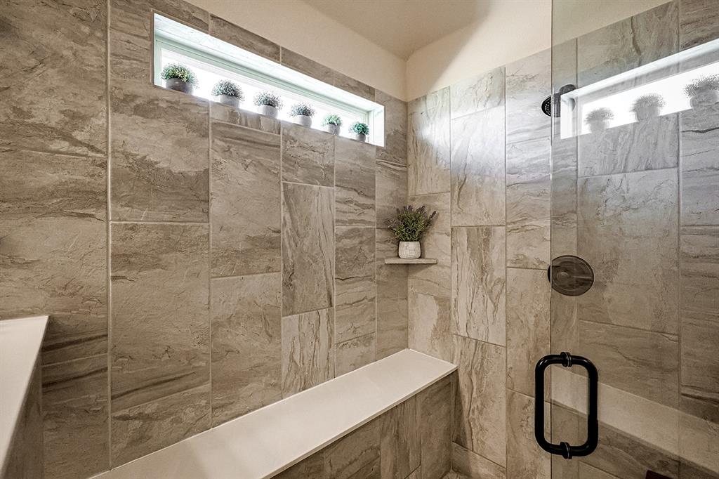 Walk-in shower featuring floor-to-ceiling stone-pattern tile, a built-in bench, integrated corner shelving, a horizontal transom window, and a frameless glass door with matte black hardware
