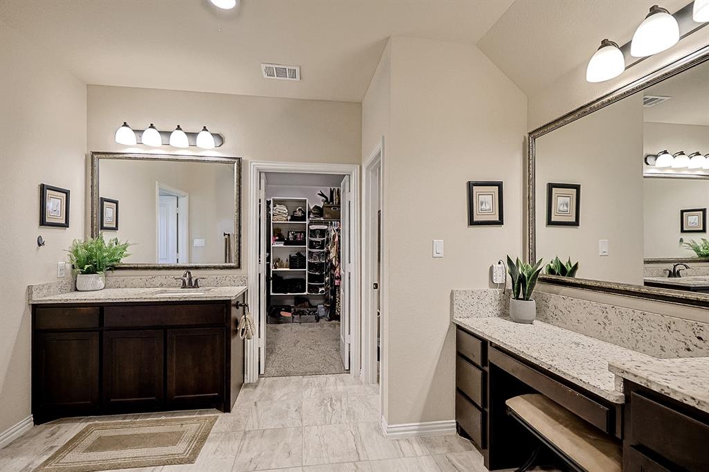 Bathroom featuring dual dark-finish vanities with stone-look countertops, large framed wall mirrors, four-light vanity fixtures, and tiled flooring