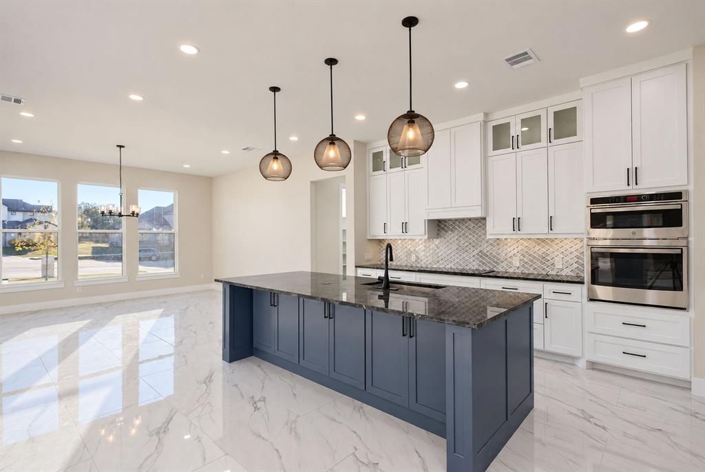 Kitchen featuring white upper cabinetry, a dark-toned center island, stone-surfaced countertops, herringbone-patterned backsplash, and integrated stainless steel double wall ovens