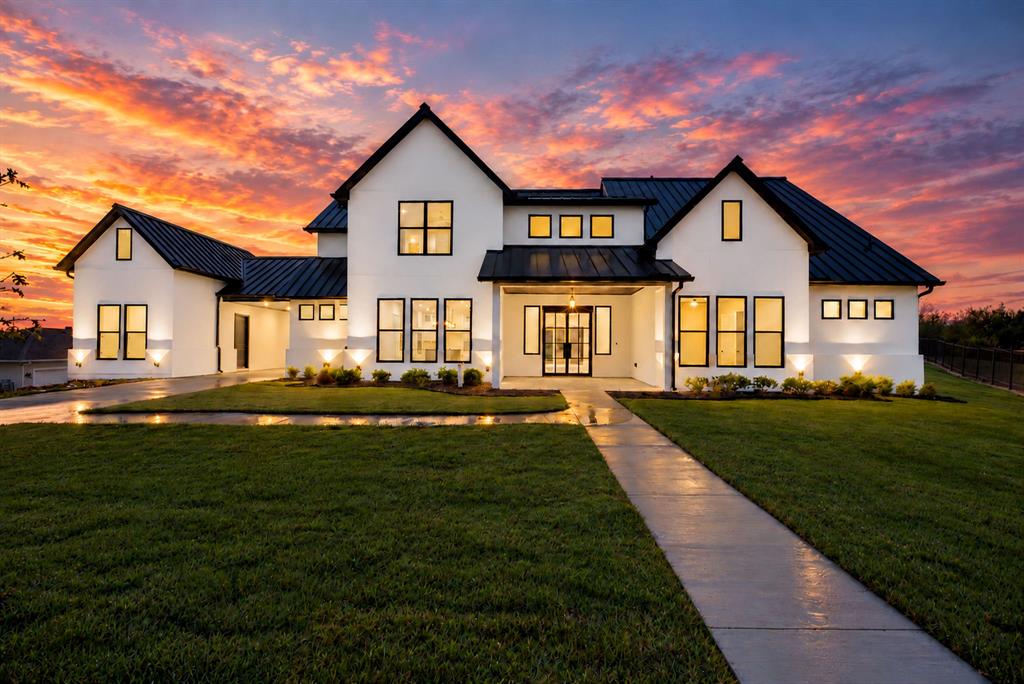 Modern farmhouse exterior featuring white stucco siding, a black metal roof, multi-pane windows with dark frames, and an integrated multi-car garage