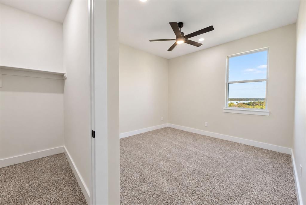 Neutral wall-to-wall carpeting, matte black ceiling fan with integrated lighting, window with exterior scenery, and built-in closet shelving