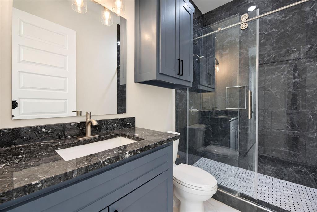Bathroom featuring dark stone countertops, a blue-painted vanity, matching overhead cabinetry, and a walk-in shower with floor-to-ceiling stone tile and a glass sliding door