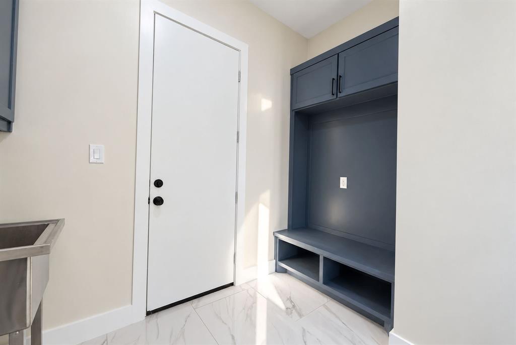 Built-in navy blue cabinetry featuring overhead storage and lower cubbies, white door with matte black hardware, and stone-finish tile flooring