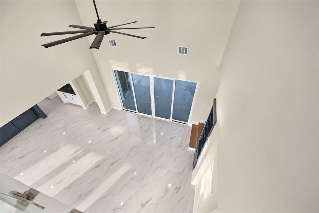 High-ceiling living area featuring large-format stone-look tile flooring, multi-panel sliding glass doors, a modern multi-blade ceiling fan, and staircase with dark metal railing