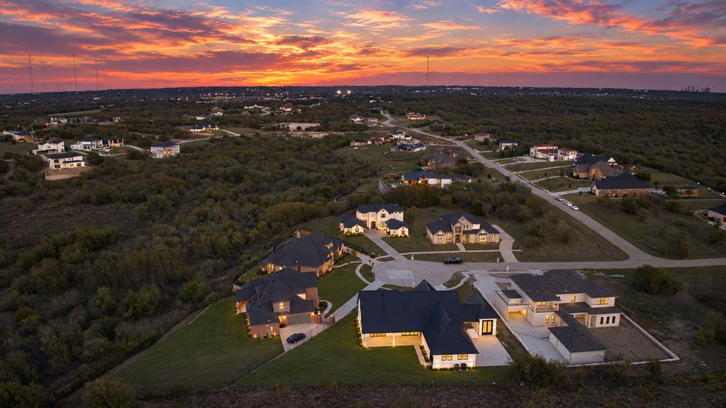 Aerial perspective featuring multi-story residential architecture, expansive lots, concrete driveways, and sunset horizon
