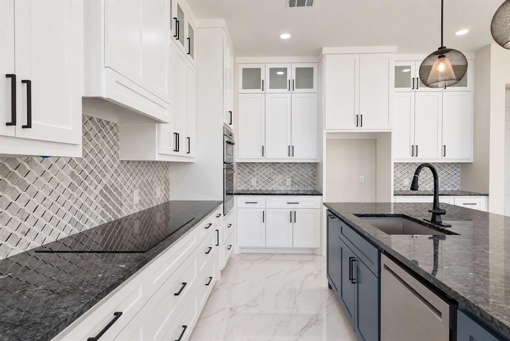 Kitchen featuring white floor-to-ceiling cabinetry, dark stone countertops, custom geometric patterned tile backsplash, polished stone-finish tile flooring, and a central island with a matte black faucet