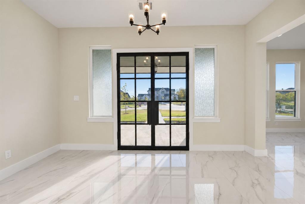 Double entry doors with black iron-style frames, fluted glass side panels, polished stone-finish flooring, and a six-light modern chandelier