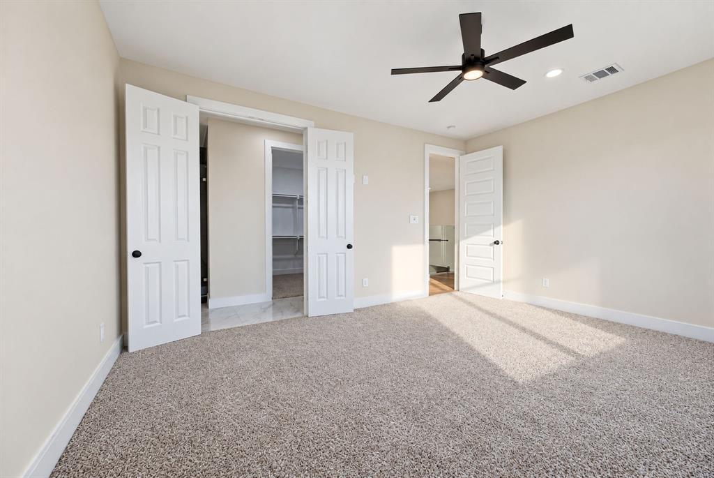 Neutral-toned interior featuring plush carpeting, a modern matte-black ceiling fan, multi-panel doors, and built-in closet shelving