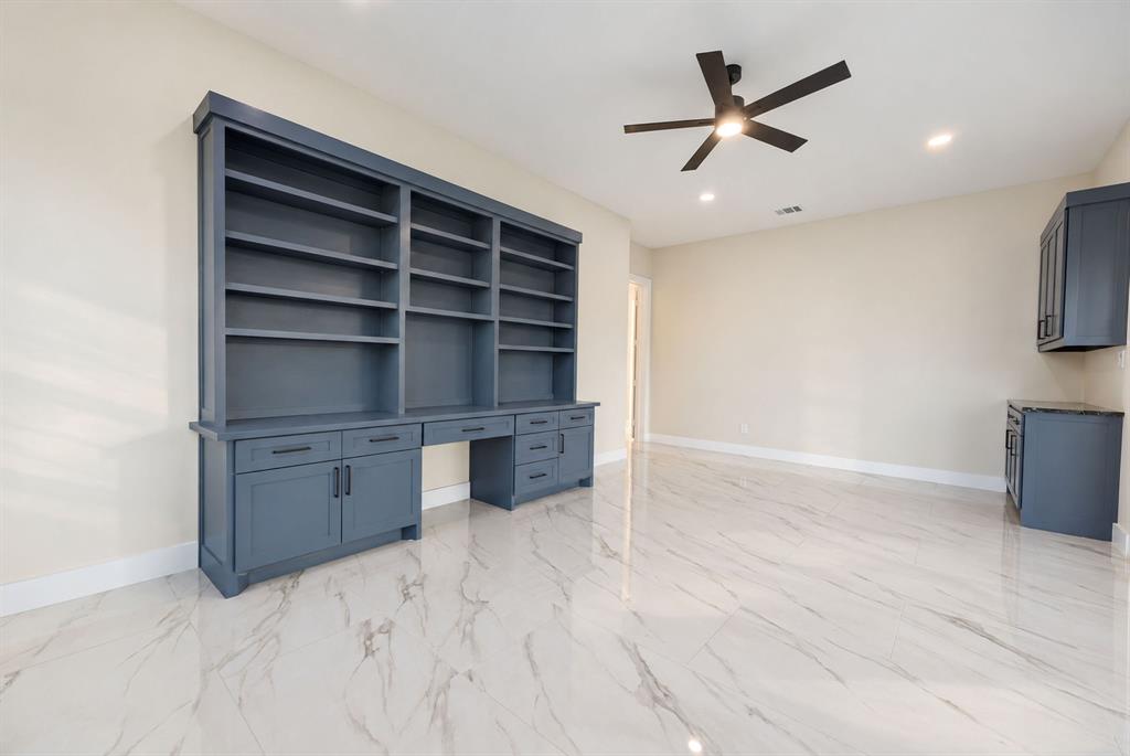 Custom built-in shelving featuring navy blue cabinetry with integrated desk space, polished stone-finish tile flooring, and a ceiling-mounted matte black light fixture