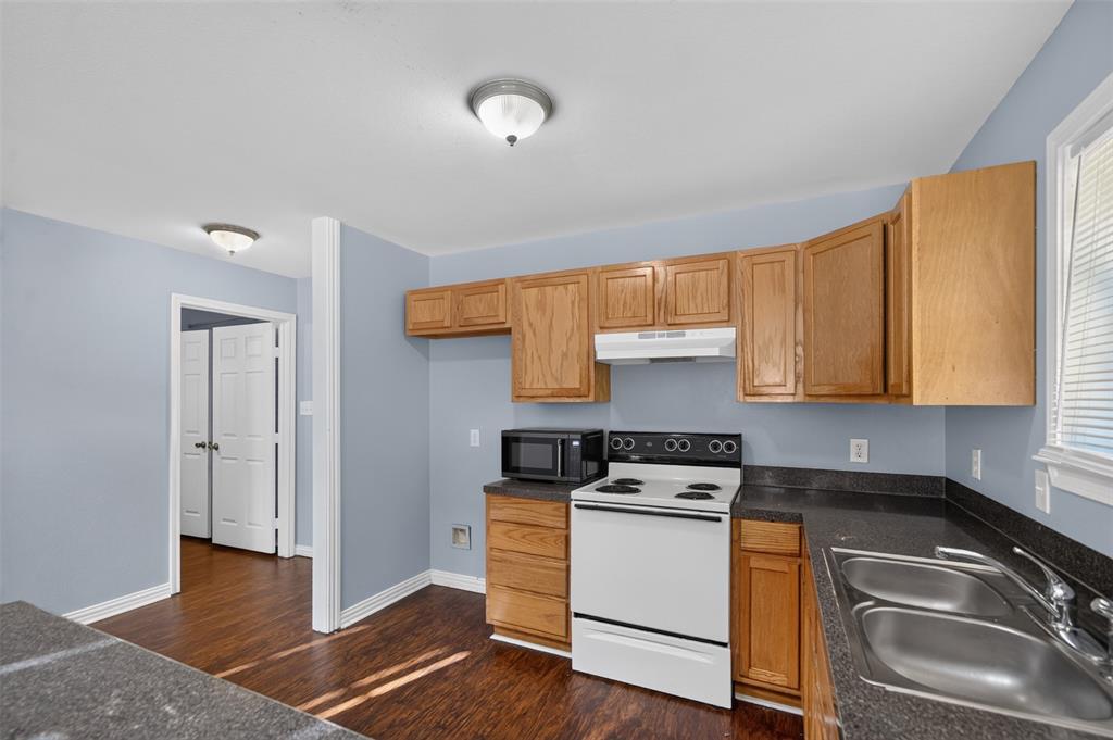 Kitchen featuring oak-finish cabinetry, dark solid-surface countertops, dual-basin stainless steel sink, electric range, and wood-finish flooring
