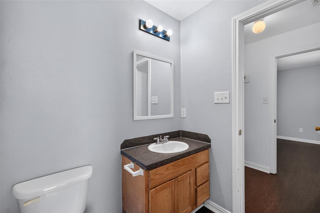 Wood-finish vanity with dark composite countertop, integrated oval basin, white-framed wall mirror, and three-bulb vanity light fixture