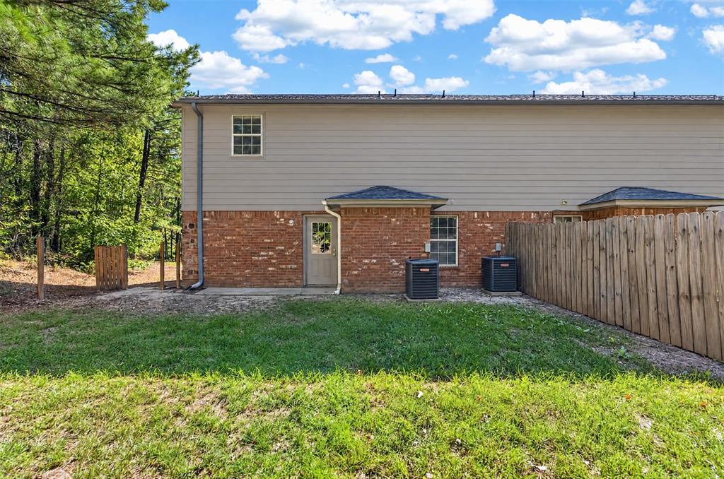 Rear exterior featuring horizontal lap siding, brick facade, wood-style privacy fencing, and two ground-level heating and cooling units