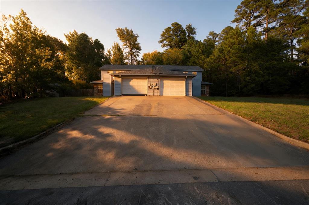 Exterior of a residence featuring a dual-bay garage, concrete driveway, and expansive lawn surrounded by mature trees Exterior of a residence featuring a dual-bay garage, concrete driveway, and expansive lawn surrounded by mature trees