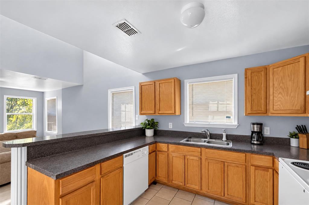 Kitchen featuring wood cabinetry, dark countertops, a double-basin sink, and tile flooring