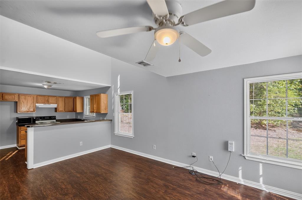 Vaulted ceiling featuring a central light fixture and ceiling fan, wood-finish flooring, dual-pane windows, and a breakfast bar