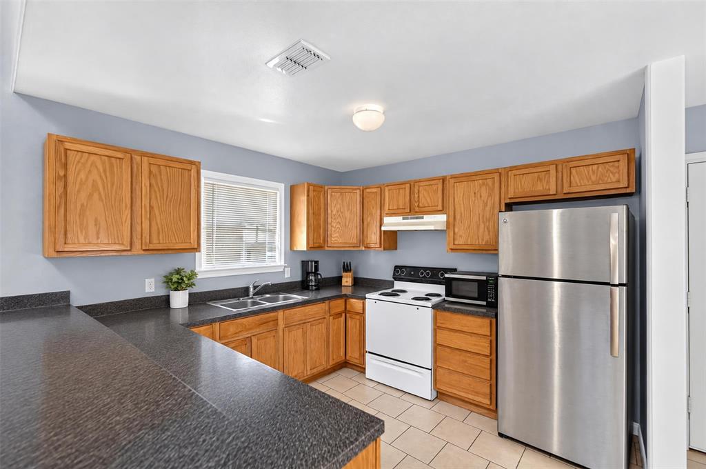 Kitchen featuring light wood cabinetry, stone-finish countertops, tile flooring, and stainless steel refrigerator