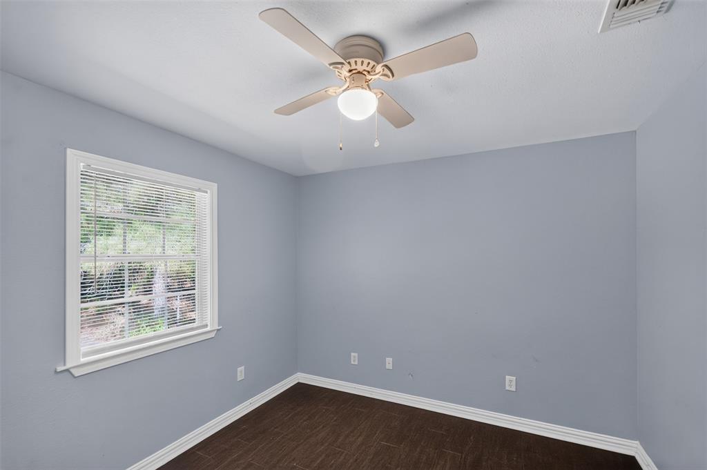 Room featuring wood-finish flooring, a multi-blade ceiling fan with an integrated light fixture, and a window with horizontal blinds