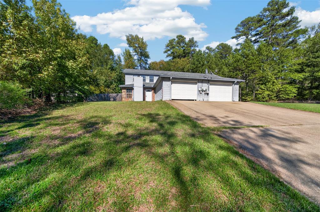 Two-story residence featuring light-toned horizontal siding, a concrete driveway, a dual-bay garage, and an exterior chimney on a wooded lot