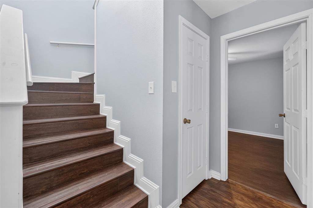 Staircase featuring wood-finish treads, white painted risers, and a wall-mounted handrail, accompanied by six-panel interior doors and wood-finish flooring
