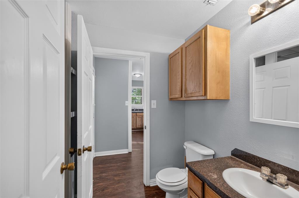 Wall-mounted natural wood cabinetry, dark-toned countertop with integrated sink, three-light vanity fixture, and white interior doors