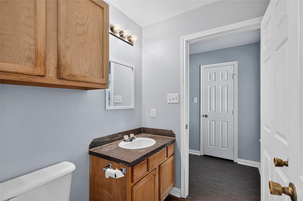 Built-in wood cabinetry, stone-finish vanity countertop with integrated sink, three-bulb vanity lighting, and wood-finish flooring