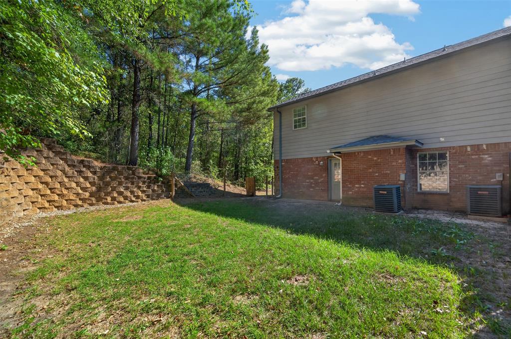 Rear exterior featuring a brick and horizontal siding facade, tiered stone retaining wall, and wooded perimeter