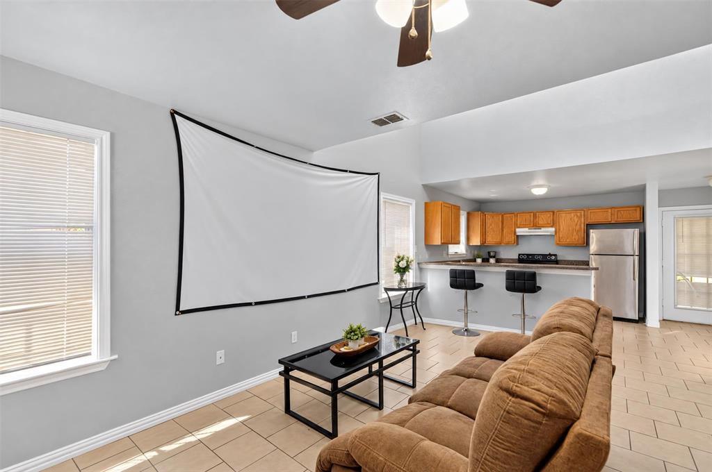 Vaulted ceilings, ceramic tile flooring, and open-concept layout featuring a kitchen breakfast bar, wood cabinetry, and stainless steel refrigerator