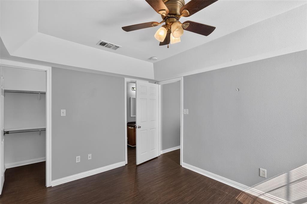 Tray ceiling with a central multi-light ceiling fan, wood-finish flooring, and a reach-in closet featuring built-in shelving