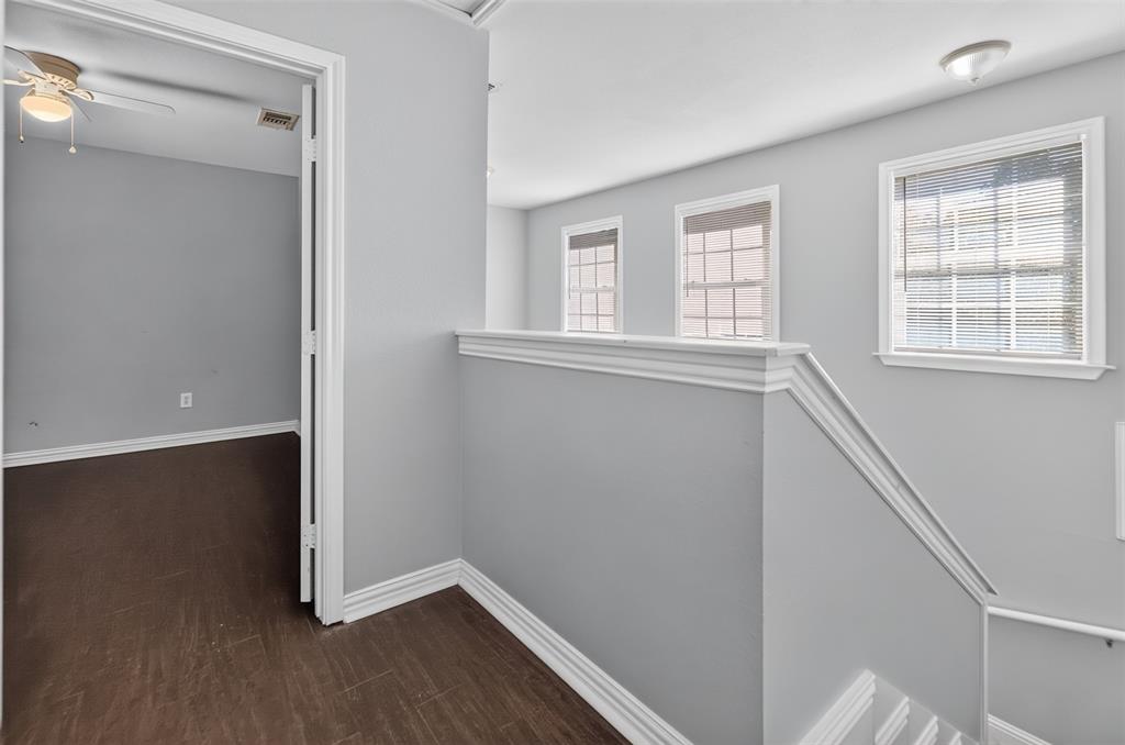 Neutral-toned interior featuring dark wood-finish flooring, multi-pane windows, decorative chair rail molding, and a ceiling fan with integrated lighting