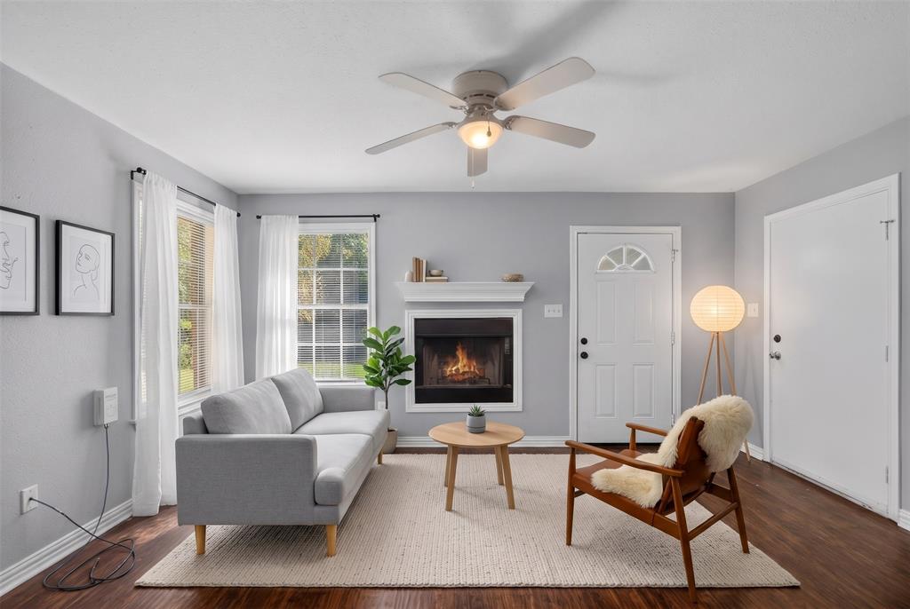 Fireplace with white mantel, wood-finish flooring, ceiling fan with integrated lighting, and multi-pane windows