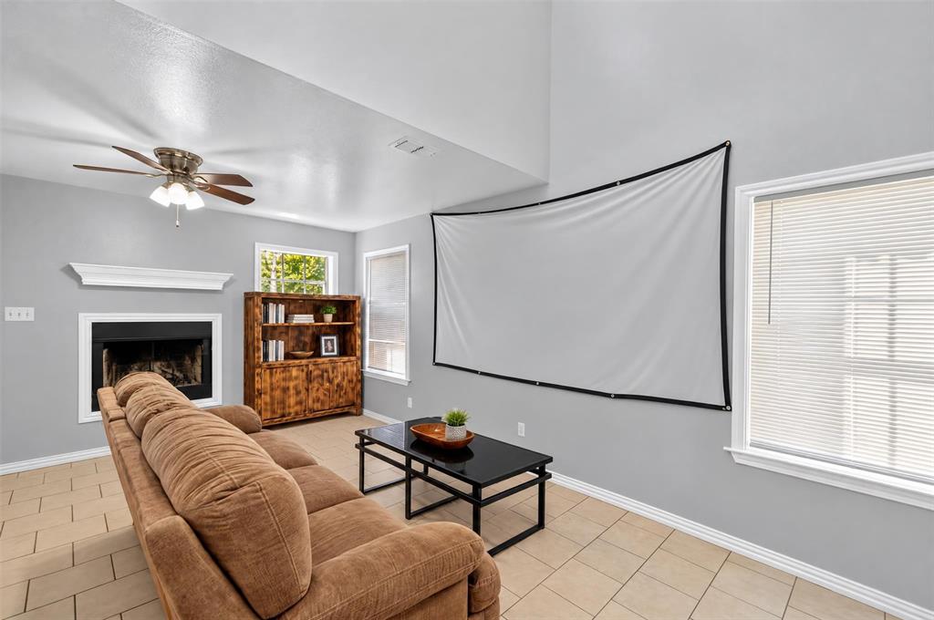 High-ceiling living space featuring a fireplace with a mantel, built-in shelving, tile flooring, and a ceiling fan