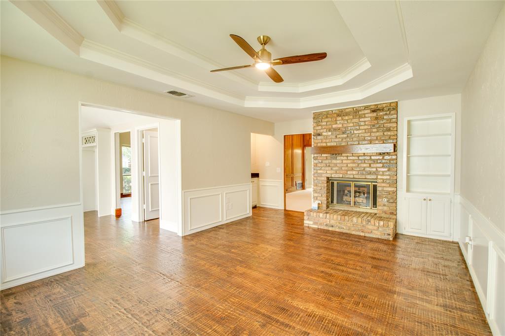Living area featuring wood-finish flooring, a tray ceiling with a ceiling fan, a floor-to-ceiling brick fireplace with a wood mantel, and built-in cabinetry with lower storage