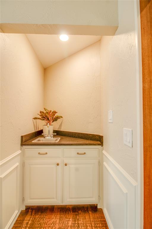 Built-in corner wet bar featuring white cabinetry, solid-surface countertop, integrated basin, and detailed wall molding
