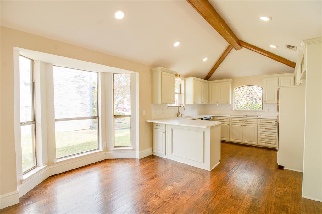 Kitchen featuring vaulted ceilings with exposed wood beams, wood-finish flooring, a bay window, recessed lighting, and a leaded glass accent window