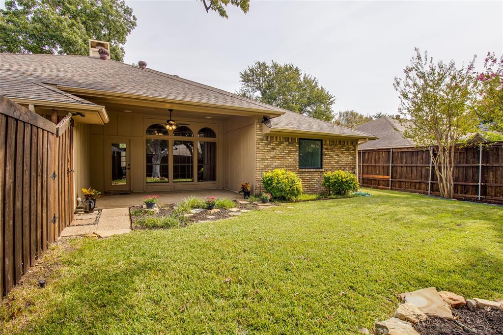 Covered concrete patio featuring an arched transom window, a ceiling fan, brick and horizontal siding exterior, and a fenced backyard with established landscaping