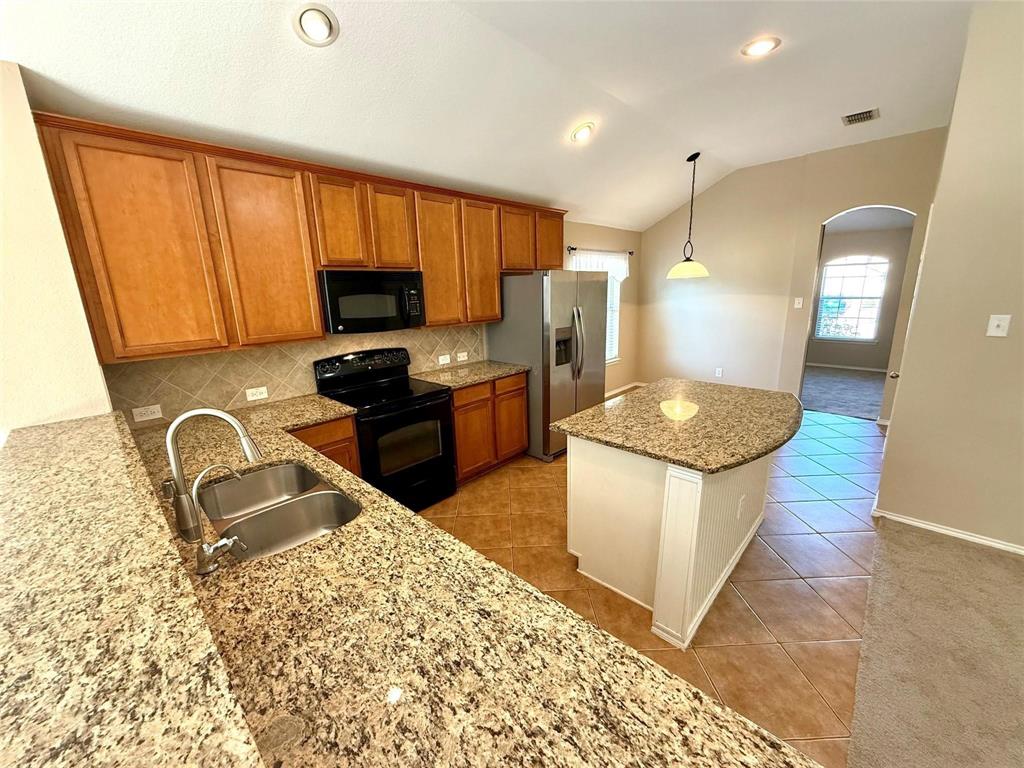 Kitchen featuring natural stone countertops, custom wood cabinetry, stainless steel appliances, a center island, and tile flooring under a vaulted ceiling Kitchen featuring natural stone countertops, custom wood cabinetry, stainless steel appliances, a center island, and tile flooring under a vaulted ceiling