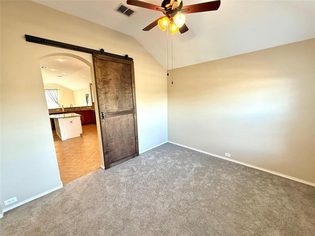 Vaulted ceiling featuring a central ceiling fan with integrated lighting, a sliding wood-finish door with black hardware, and neutral wall-to-wall carpeting