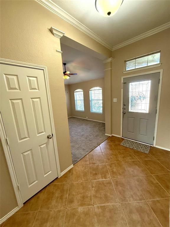 Entryway featuring tile flooring, crown molding, a decorative glass-panel front door with transom window, and architectural column detailing Entryway featuring tile flooring, crown molding, a decorative glass-panel front door with transom window, and architectural column detailing