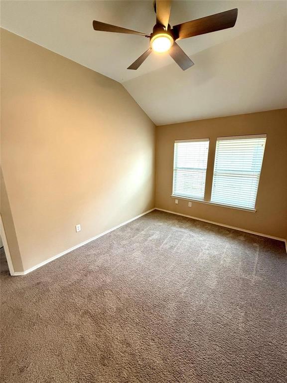 Room with vaulted ceilings, carpeting, dual windows with horizontal blinds, and an integrated ceiling fan with light fixture
