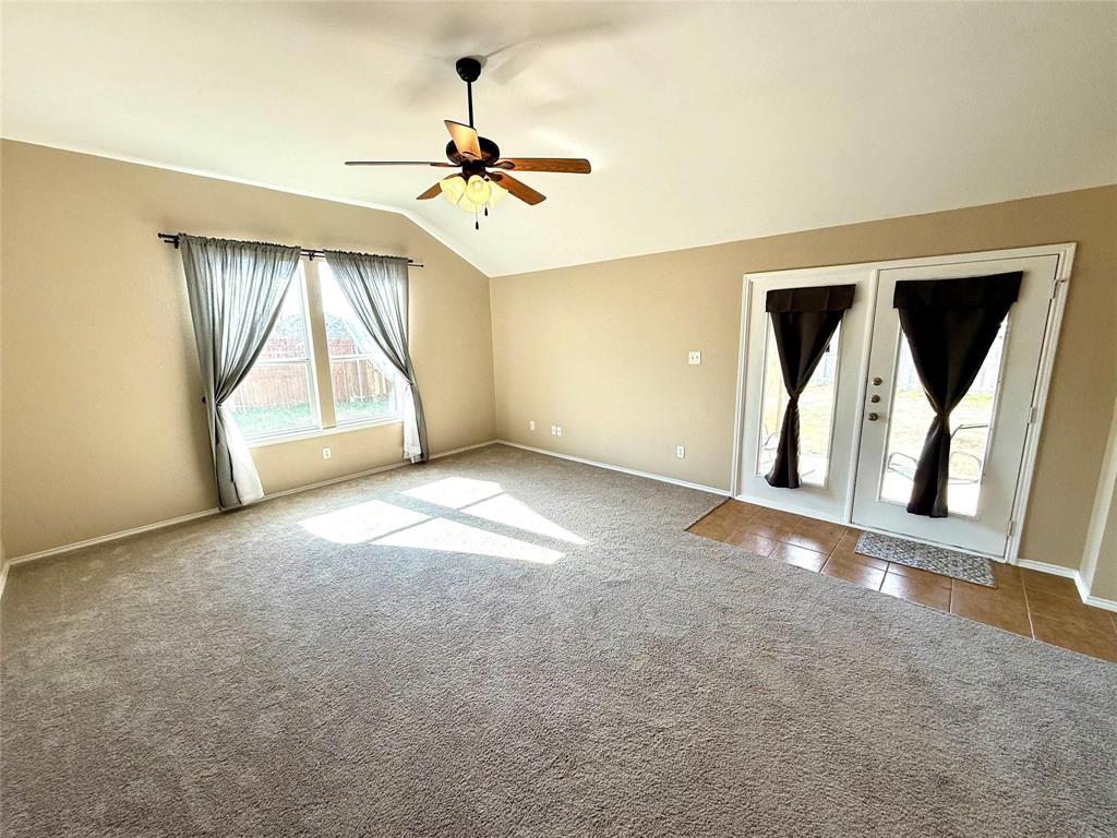 Vaulted ceilings, carpeted flooring, ceiling fan with light fixture, large windows, and glass-paneled double doors with tiled flooring