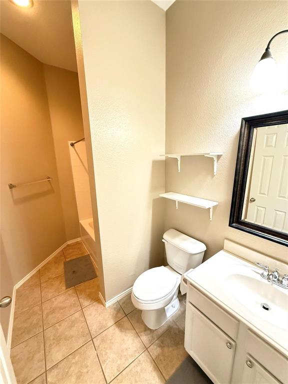 Bathroom featuring ceramic tile flooring, a white vanity with an integrated sink, dual wall-mounted storage shelves, and a tub-shower combination Bathroom featuring ceramic tile flooring, a white vanity with an integrated sink, dual wall-mounted storage shelves, and a tub-shower combination