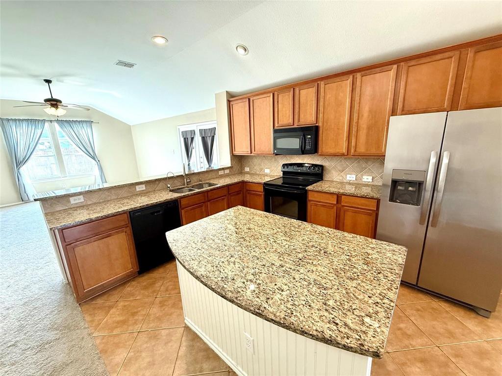 Kitchen featuring a center island, stone-patterned countertops, stainless steel appliances, stained cabinetry, and tile flooring Kitchen featuring a center island, stone-patterned countertops, stainless steel appliances, stained cabinetry, and tile flooring