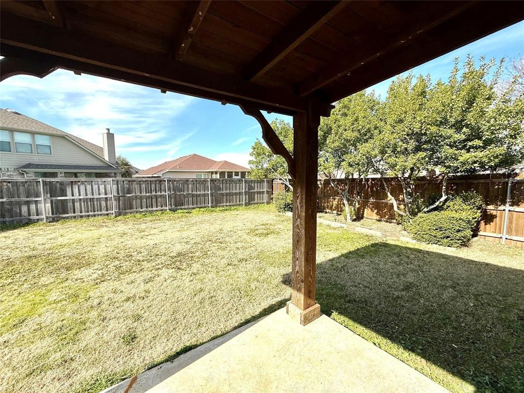 Covered outdoor patio featuring a stained wood support beam, concrete flooring, and a fenced backyard with mature trees